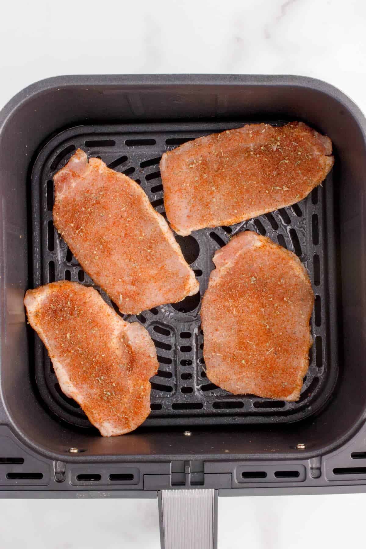 Thin pork chops arranged in a single layer in the air fryer basket.