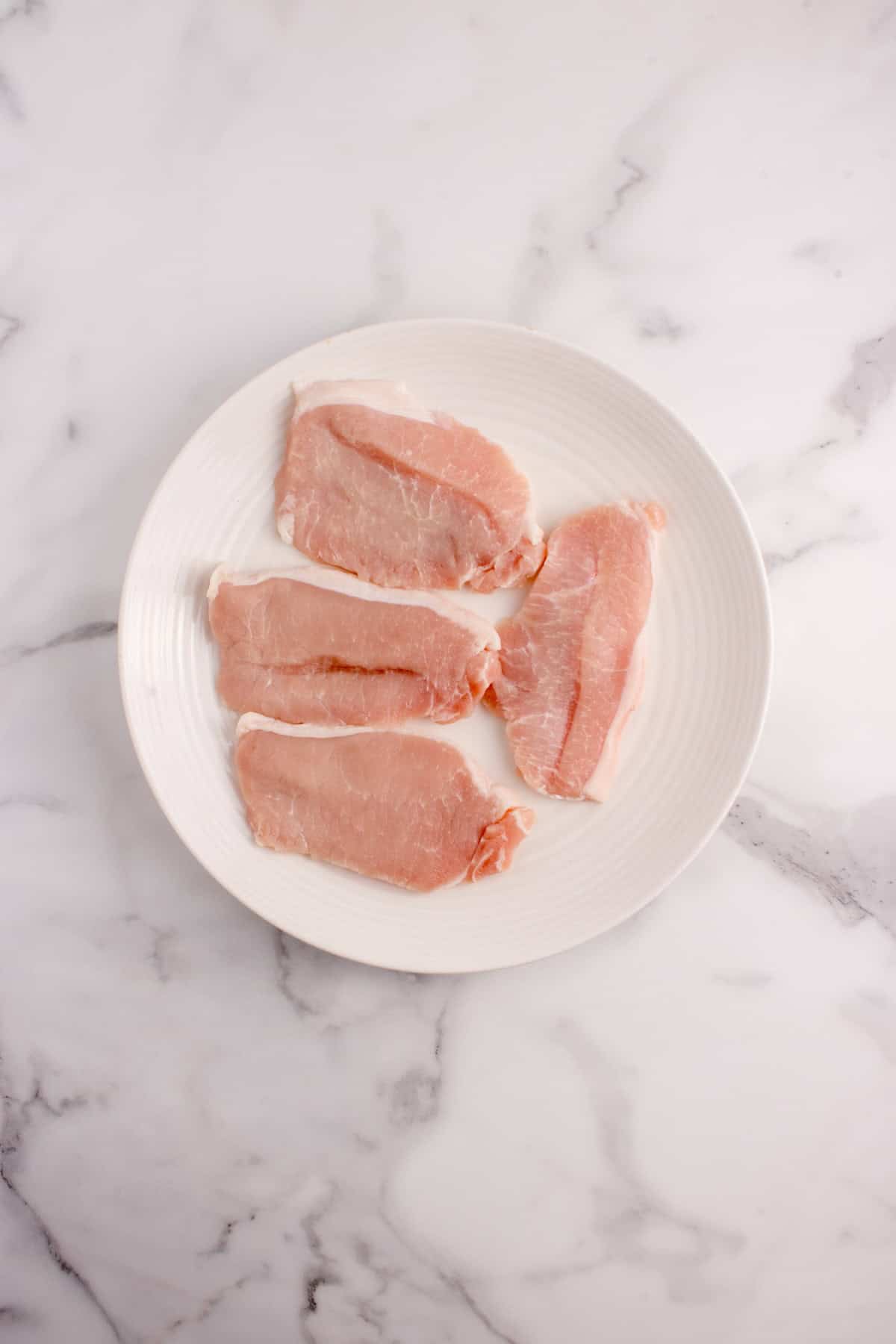 Pork chops patted dry with a paper towel on a plate.