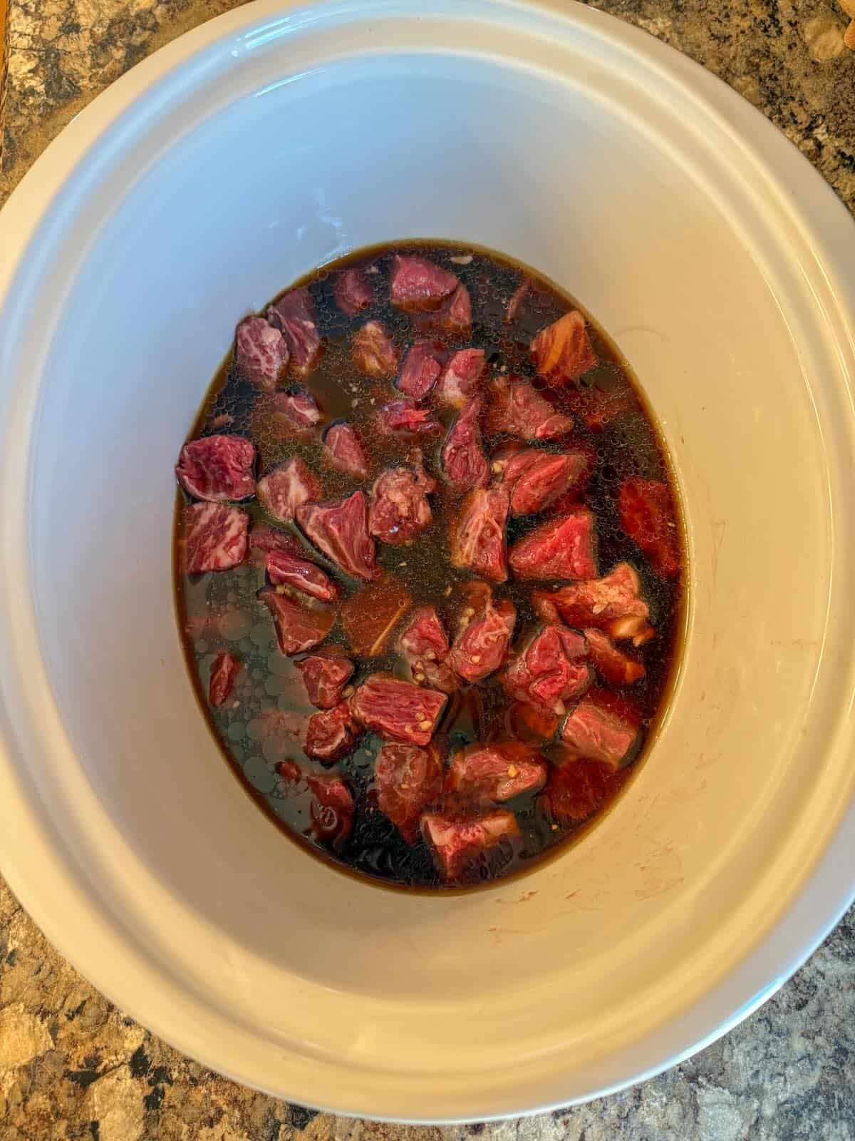 Sliced beef and soy garlic sauce mixture in a slow cooker before cooking.