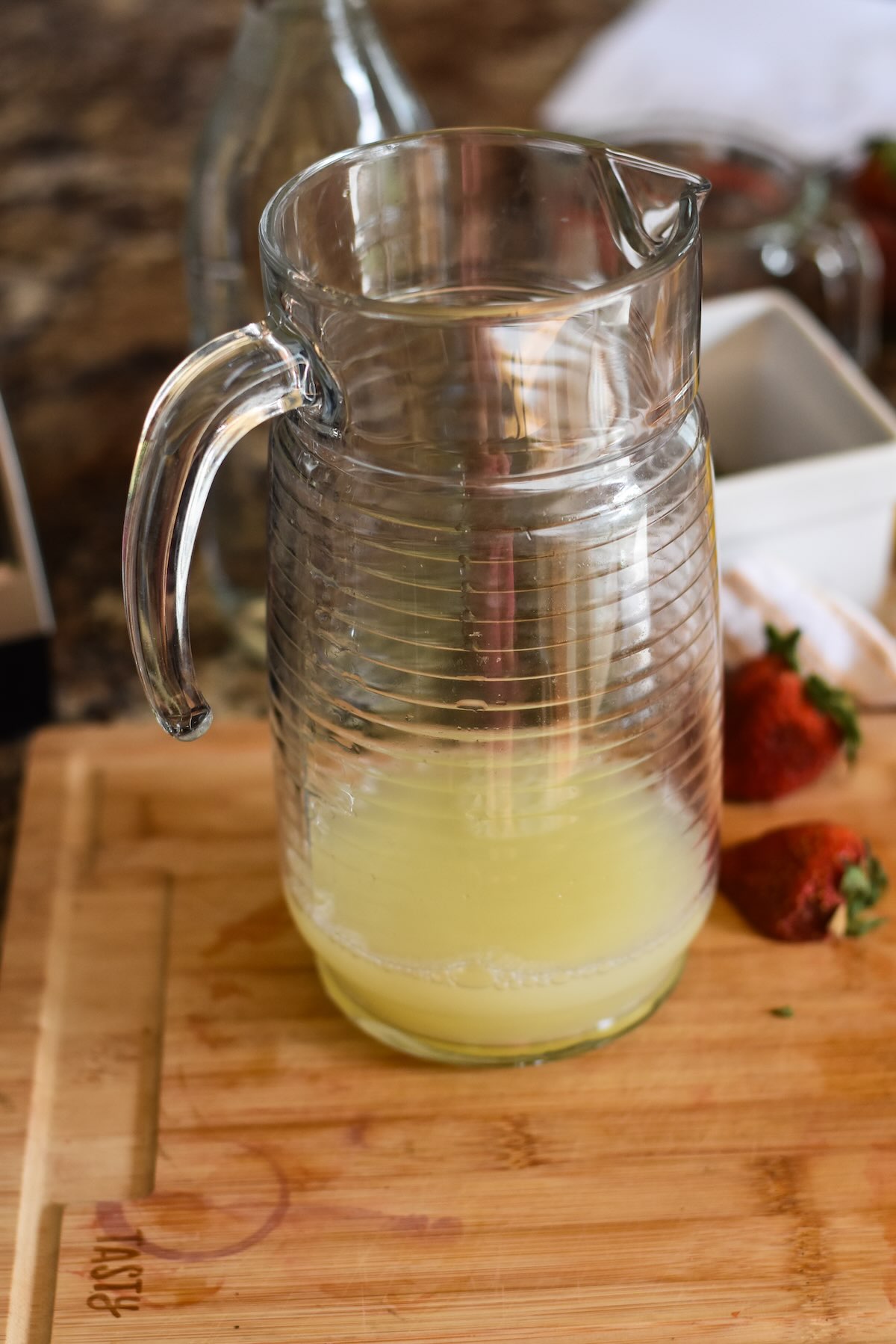 Lemon juice in a pitcher to be made into lemonade with strawberries.