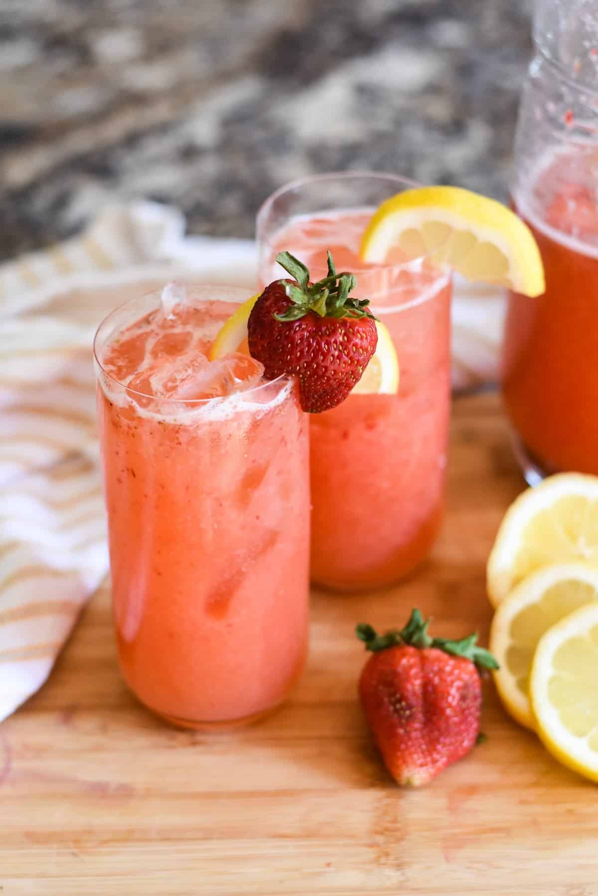 Glasses of homemade strawberry lemonade on a cutting board.