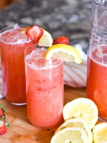 Glasses of strawberry lemonade topped with sliced fruit.