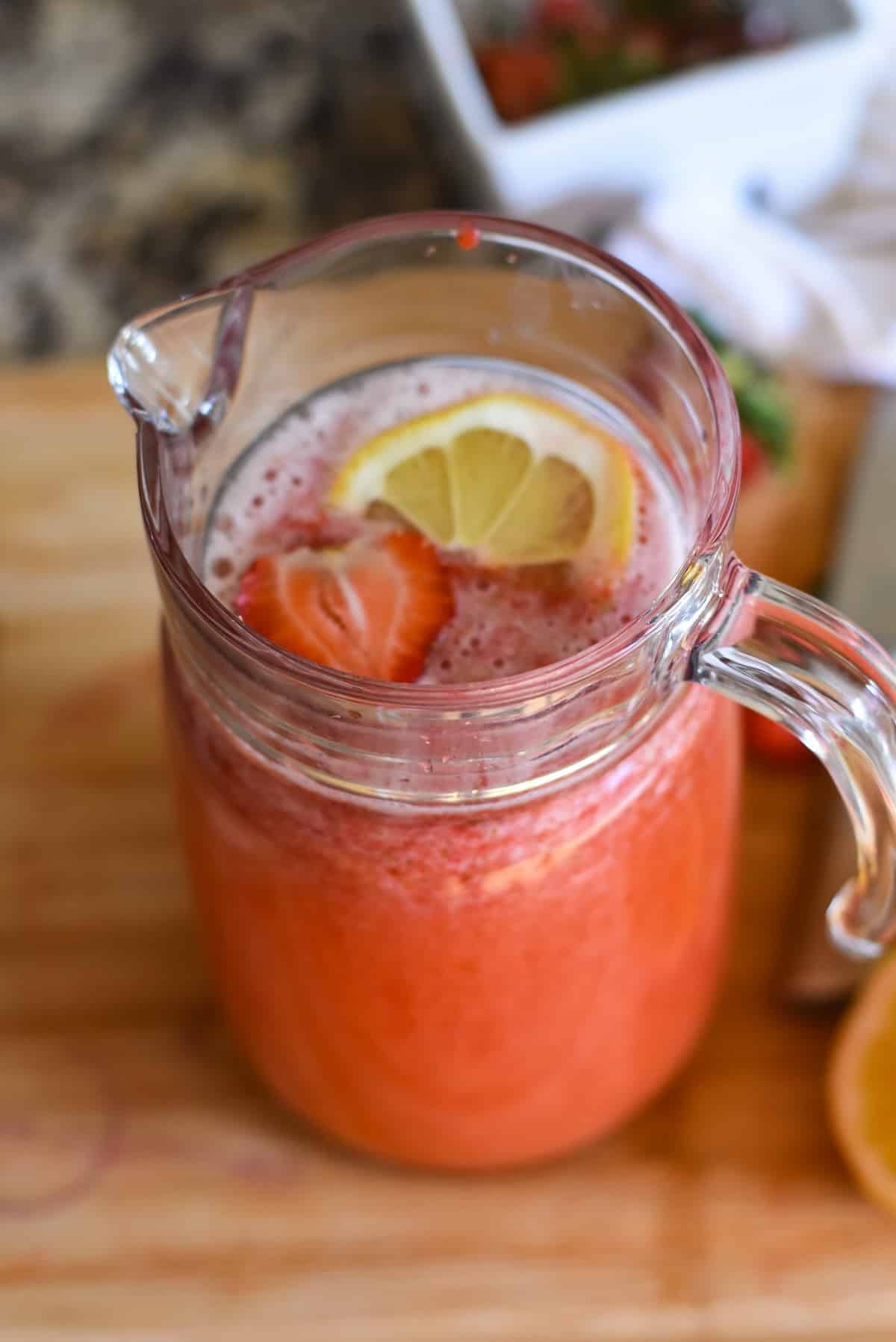 A pitcher of homemade strawberry lemonade garnished with fresh fruit.