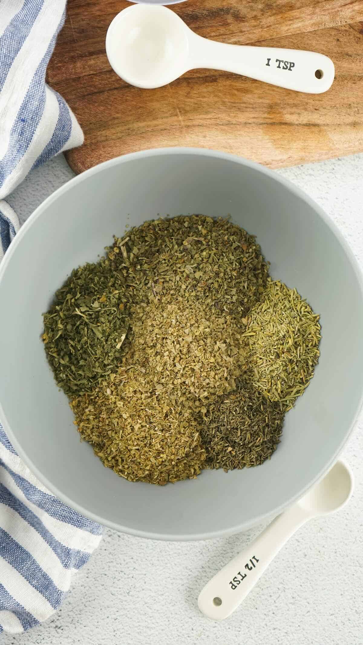 Overhead view of dried herbs like oregano, basil, and rosemary portioned into a bowl to make Italian seasoning.