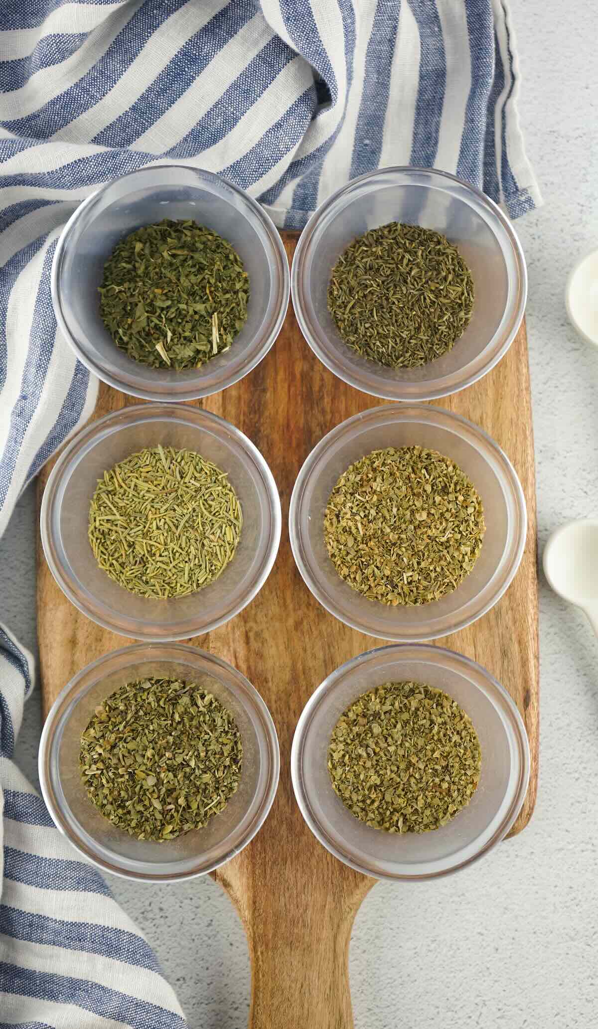 Overhead view of dried herbs like oregano, basil, and rosemary arranged in bowls for homemade Italian seasoning.