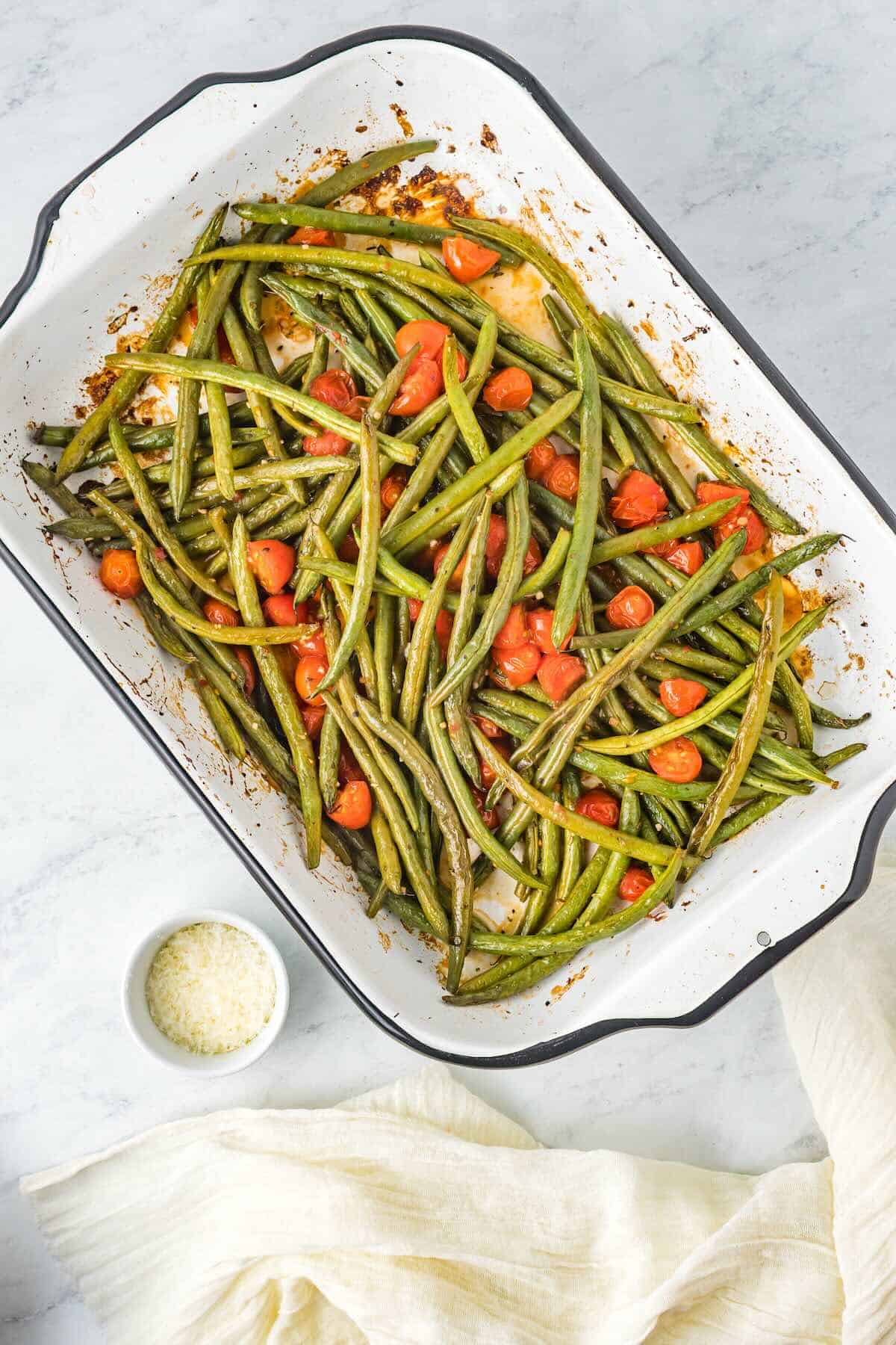 “Italian green beans roasting in the oven with halved tomatoes for a flavorful side dish.