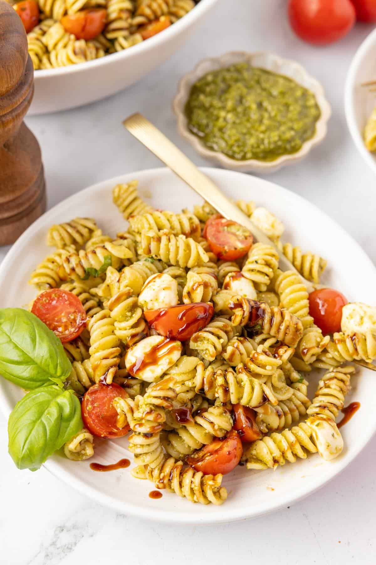 Rotini pasta salad with tomatoes, pesto and mozzarella garnished with fresh basil leaves.