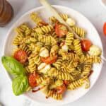 A serving of Caprese pasta salad on a white plate with a fork and fresh basil garnish.