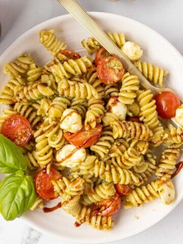 A serving of Caprese pasta salad on a white plate with a fork and fresh basil garnish.