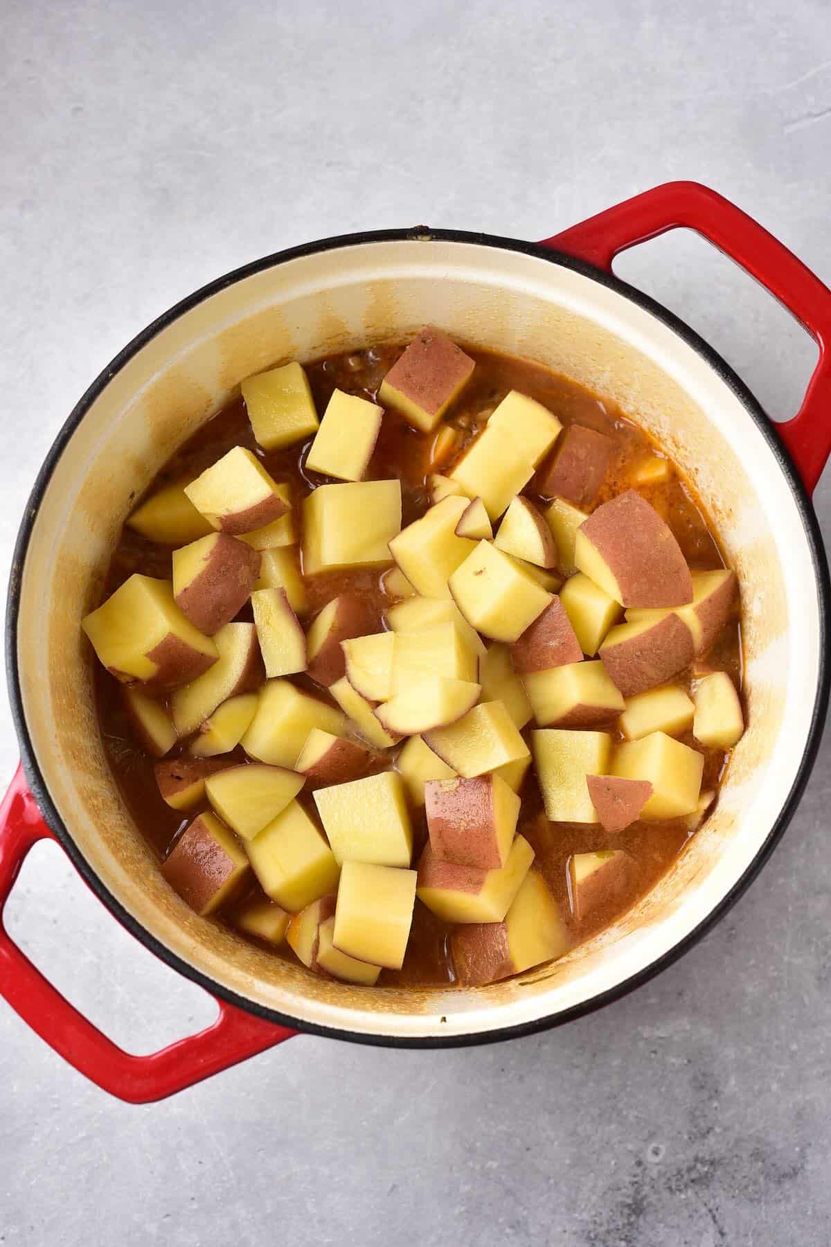 Adding chopped red potatoes into simmering venison stew.