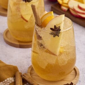Glass of apple cider punch garnished with fresh apple slices and a cinnamon stick.