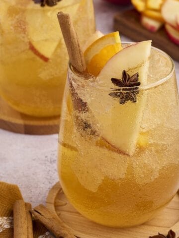 Glass of apple cider punch garnished with fresh apple slices and a cinnamon stick.