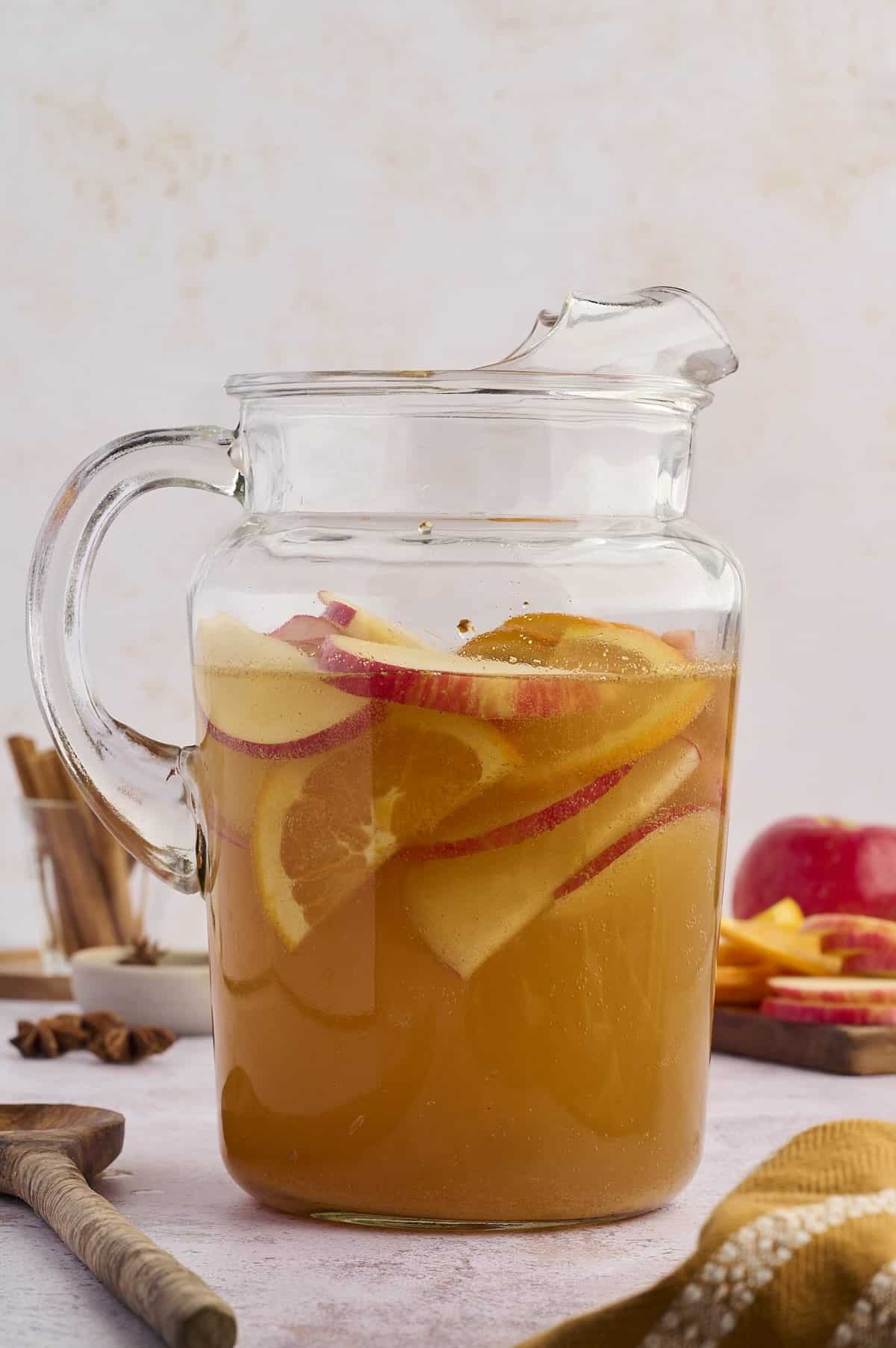 Apple cider punch served in a glass pitcher with citrus slices and cinnamon sticks.