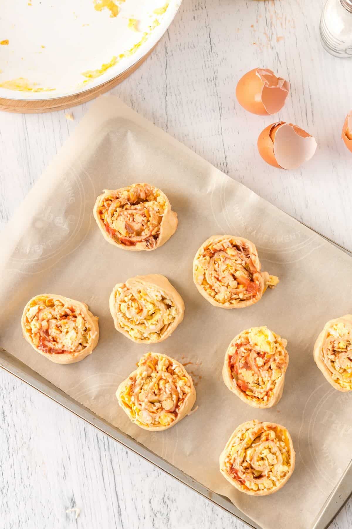 Breakfast pinwheels sliced into 8 portions on a baking sheet lined with parchment paper.