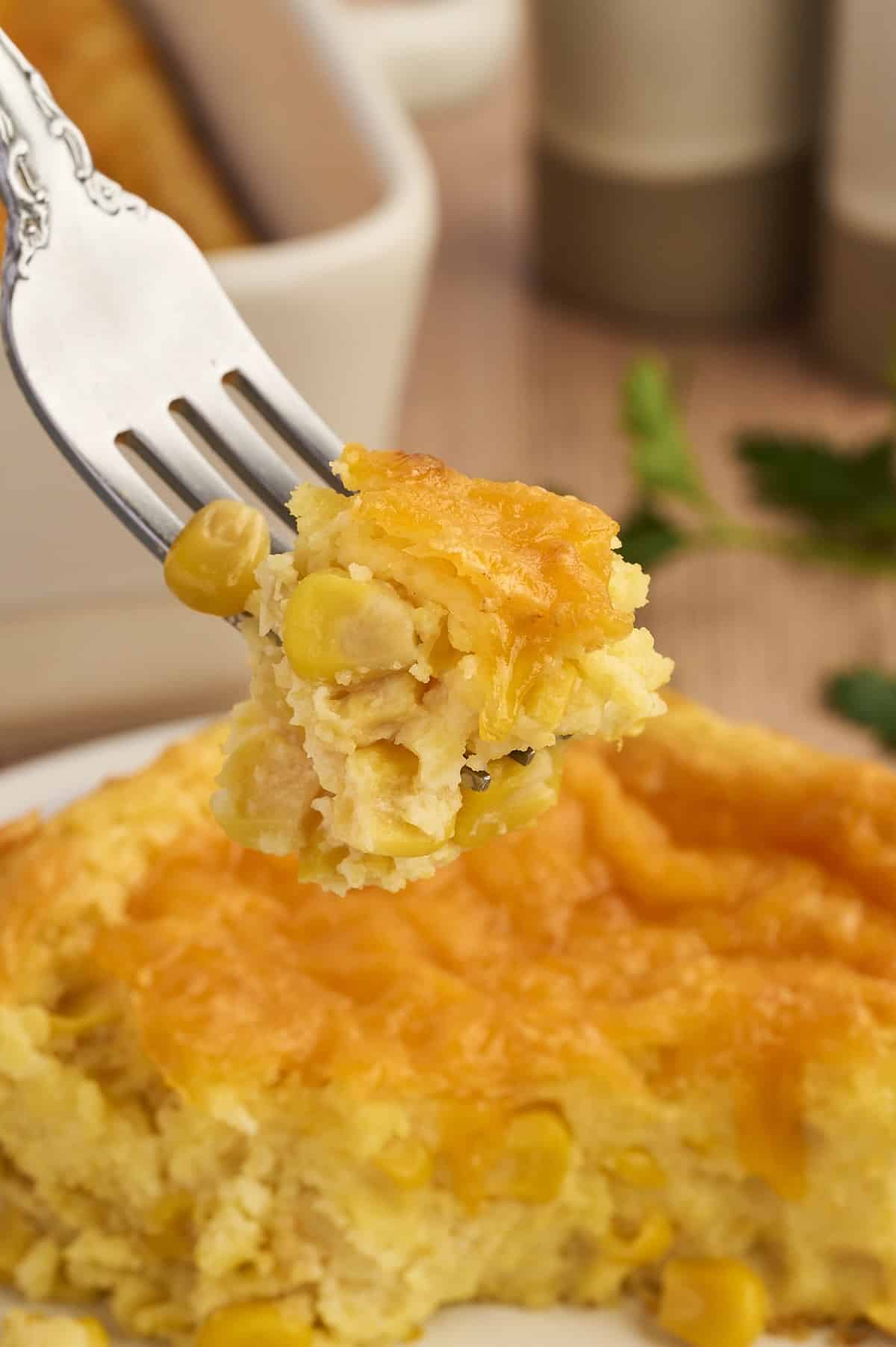 A forkful of cheesy corn casserole showing creamy texture and melted cheese.