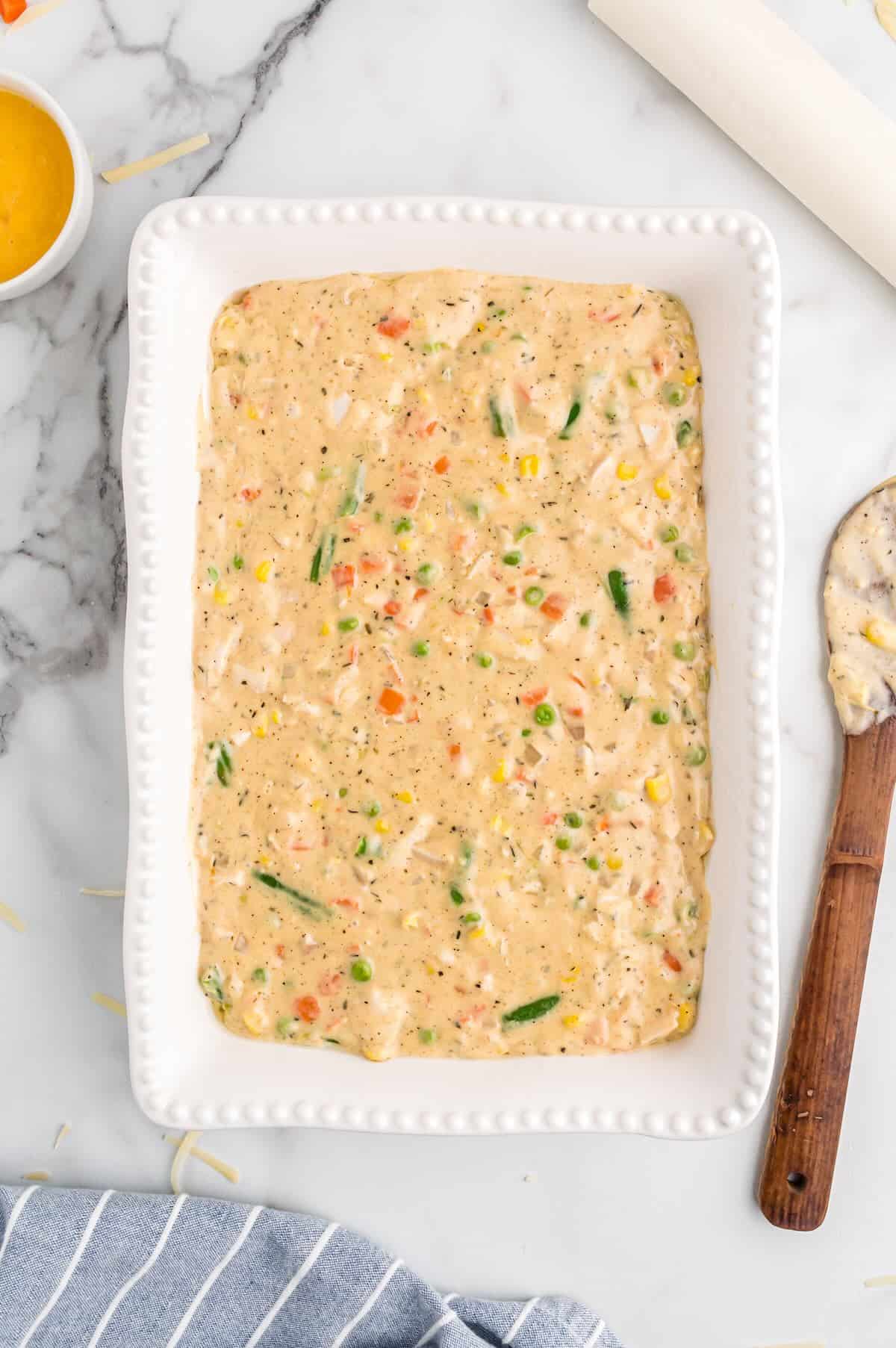 Creamy chicken mixture with vegetables spread evenly in a casserole dish.