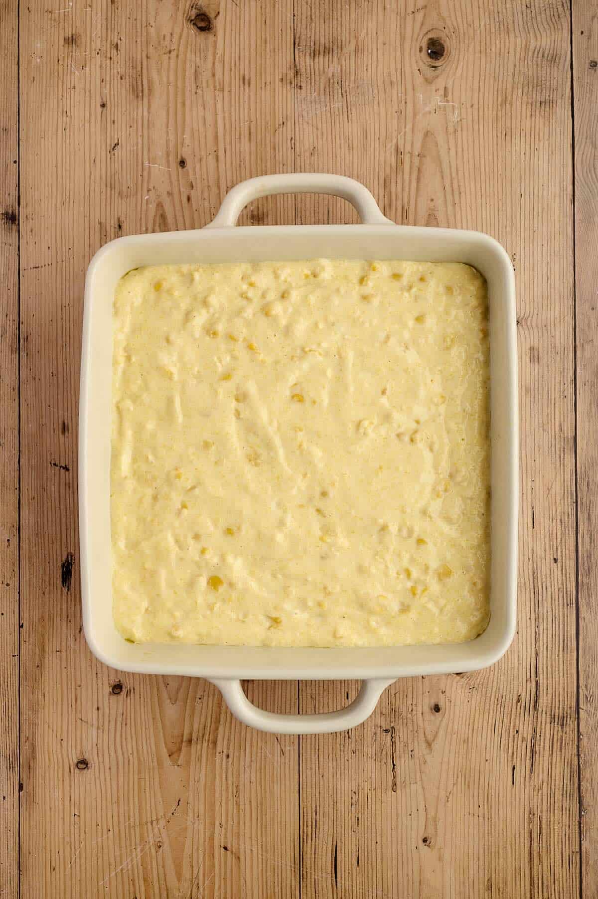 Corn casserole mixture spread evenly in a casserole dish before baking.