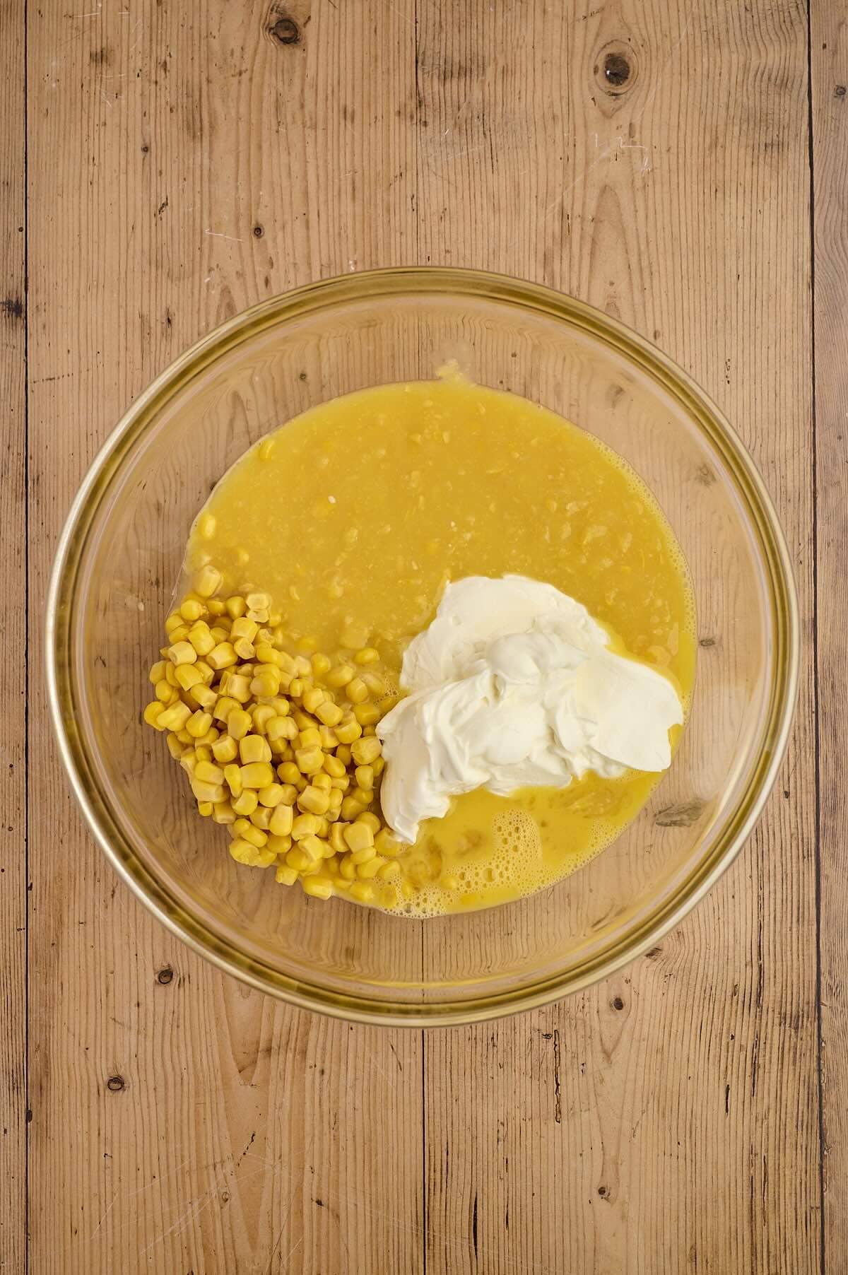 Creamed corn, corn kernels and sour cream in a glass mixing bowl.