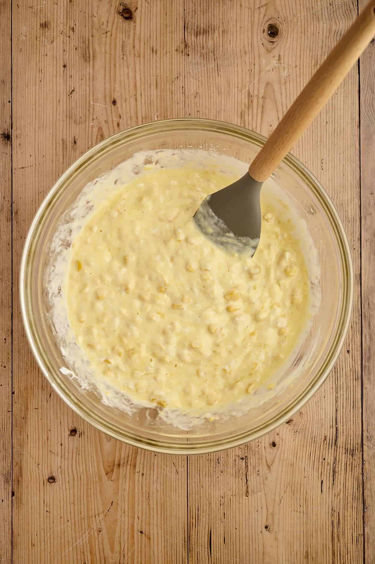 Corn casserole combined with cornbread mix in a bowl.