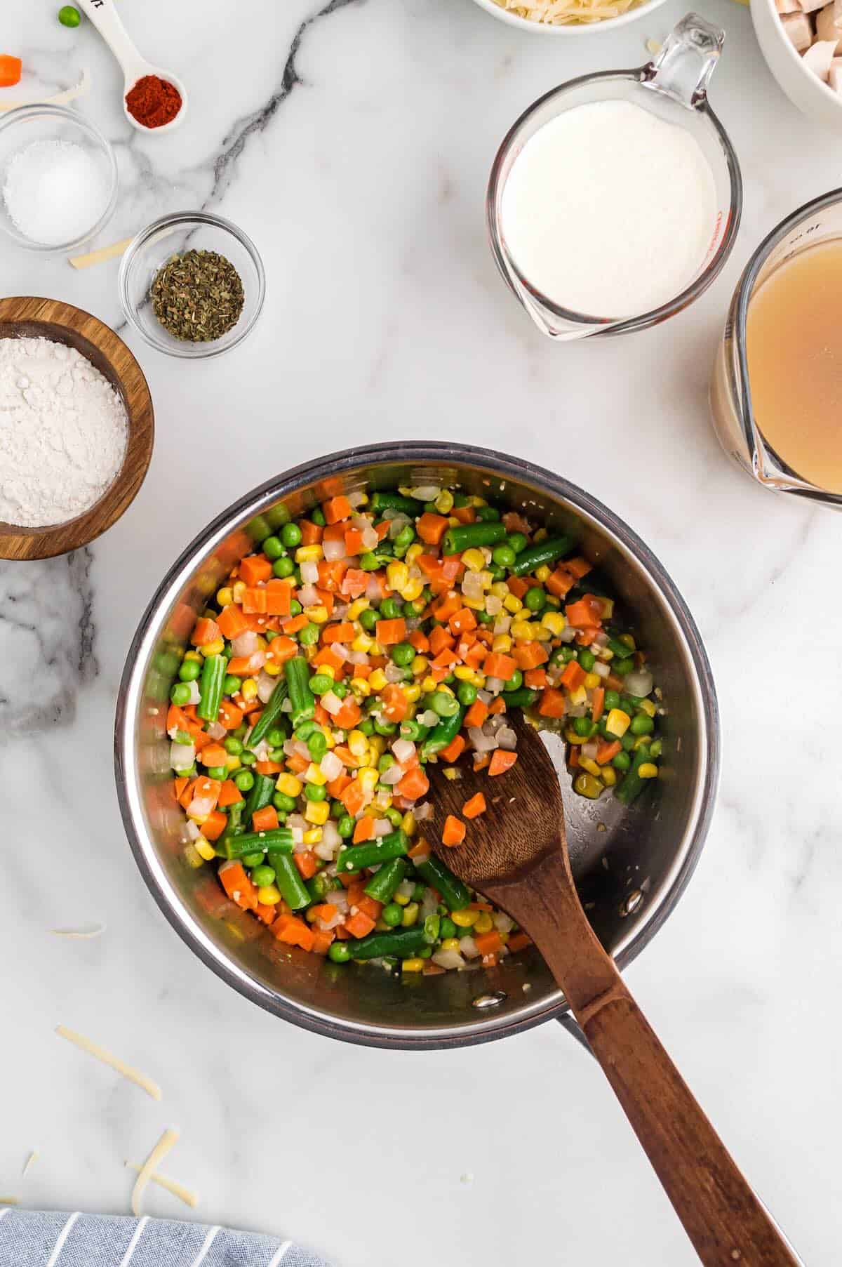 Onion and frozen mixed vegetables sautéing in a large skillet with melted butter.