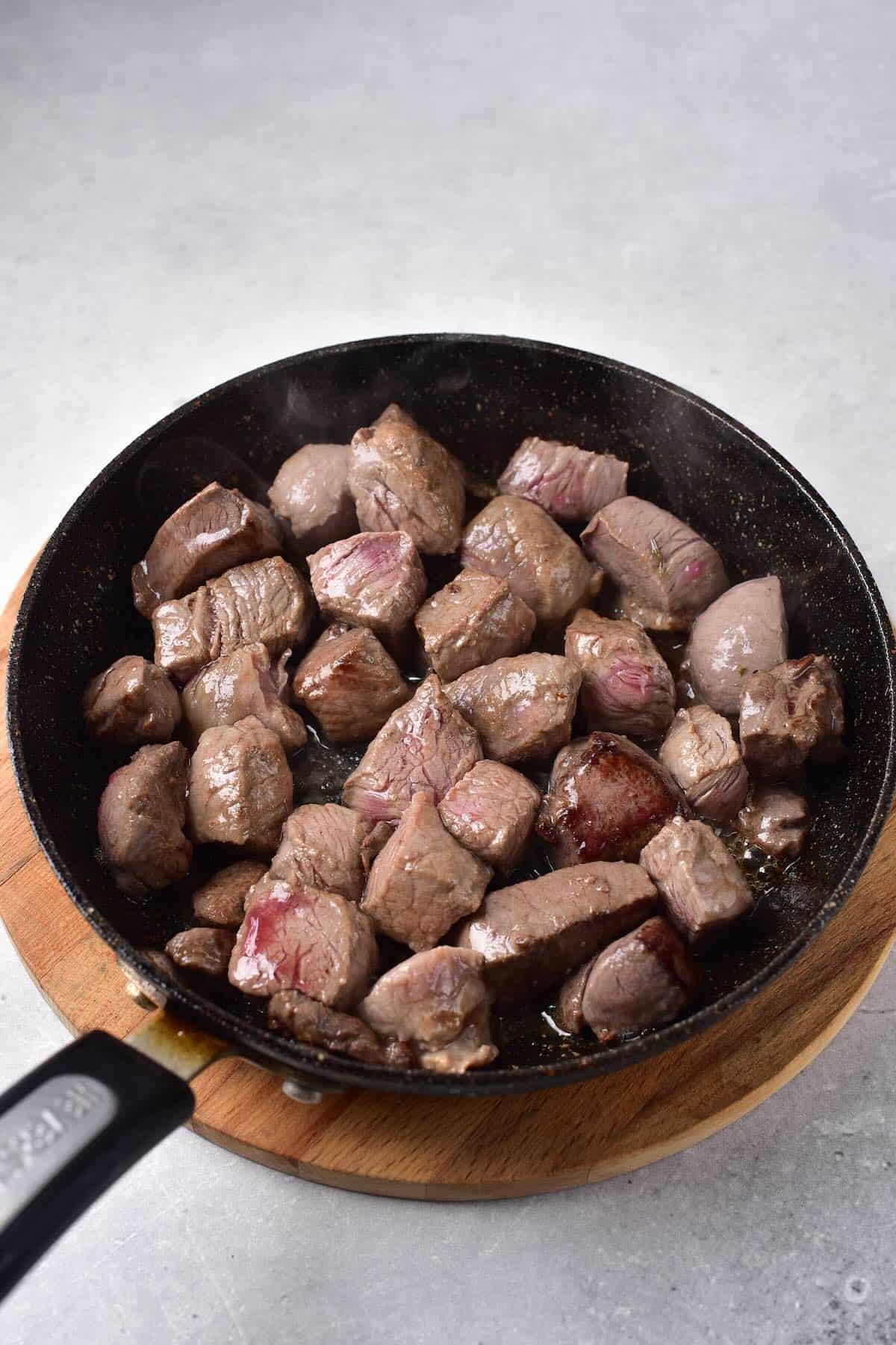 Searing venison cubes in a cast iron skillet to lock in flavor.
