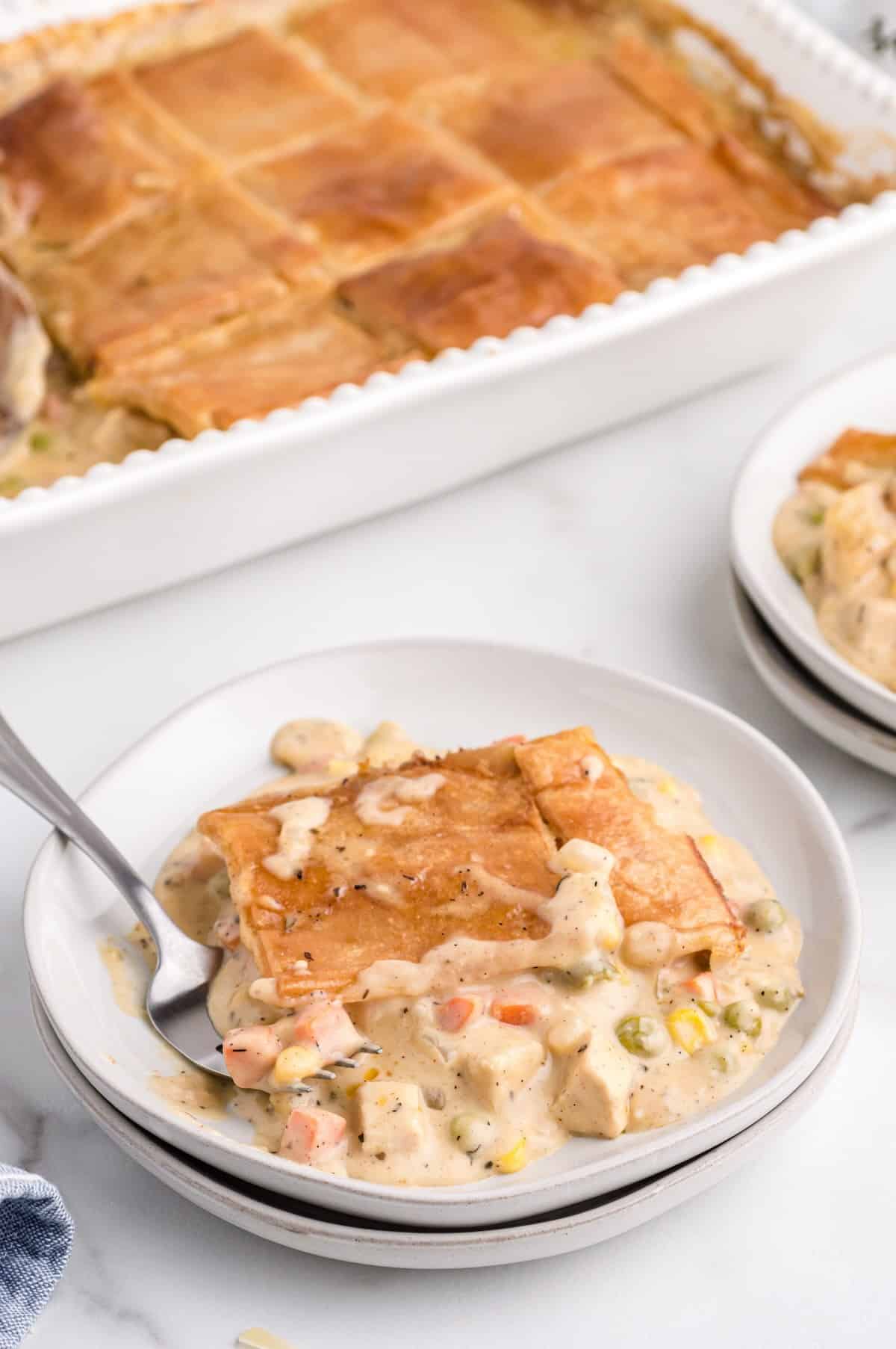 Serving a portion of chicken pot pie on a white plate, showing creamy filling and flaky crust.