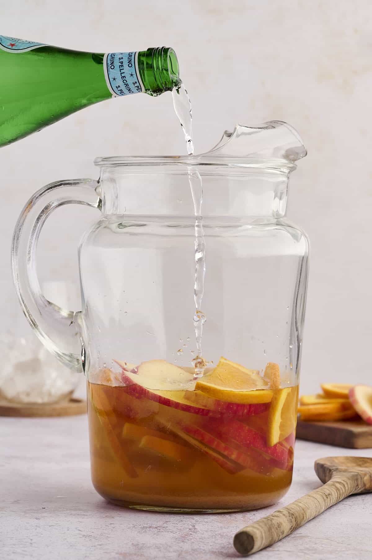 Sparkling water being poured into a pitcher of apples and fruit.