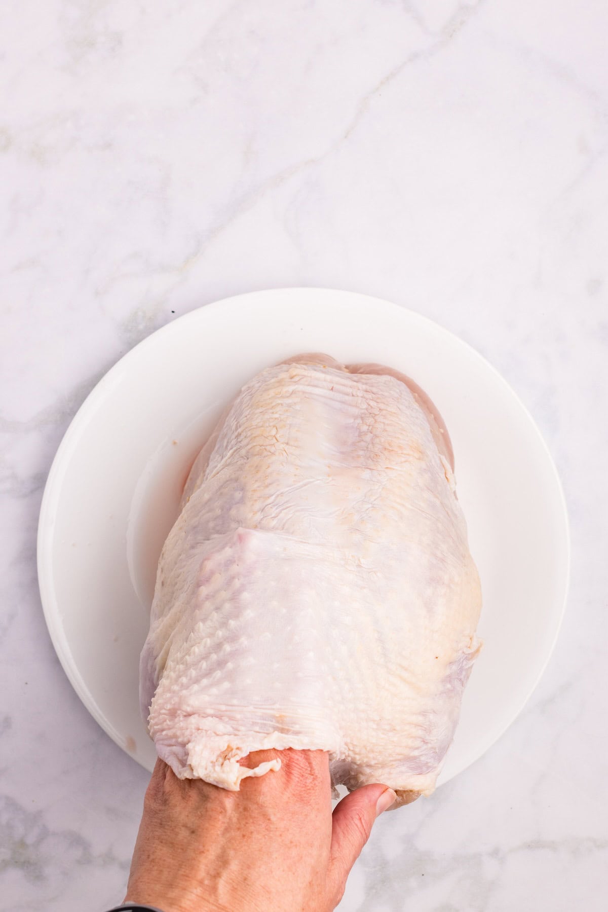 Hand loosening the skin of a bone-in turkey breast to spread herb butter directly on the meat for extra flavor and moisture.