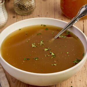 Creamy homemade chicken broth in a white bowl, garnished with herbs, on rustic wooden table for comfort food.