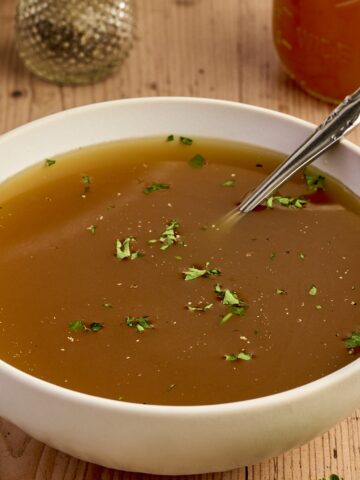 Creamy homemade chicken broth in a white bowl, garnished with herbs, on rustic wooden table for comfort food.