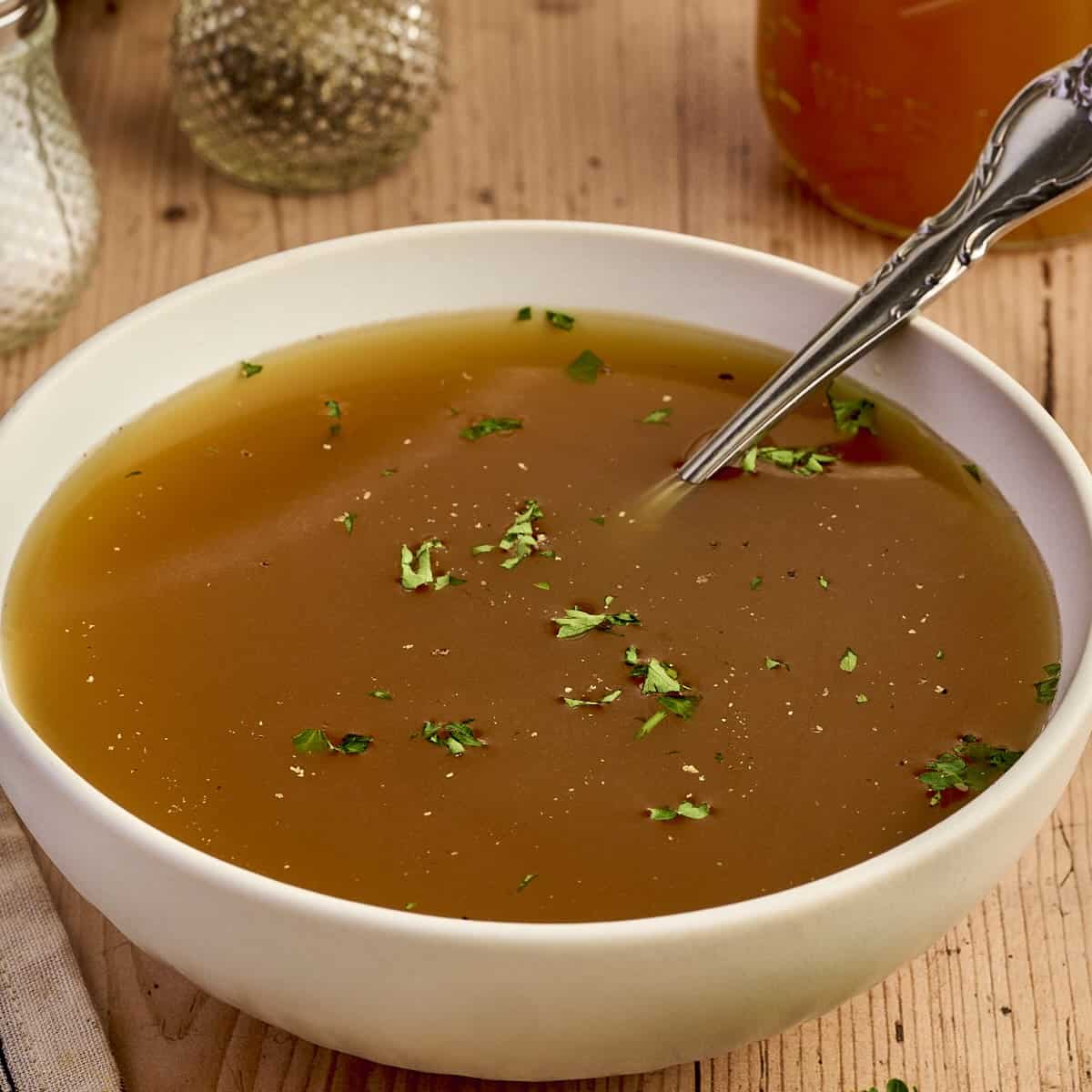 Creamy homemade chicken broth in a white bowl, garnished with herbs, on rustic wooden table for comfort food.