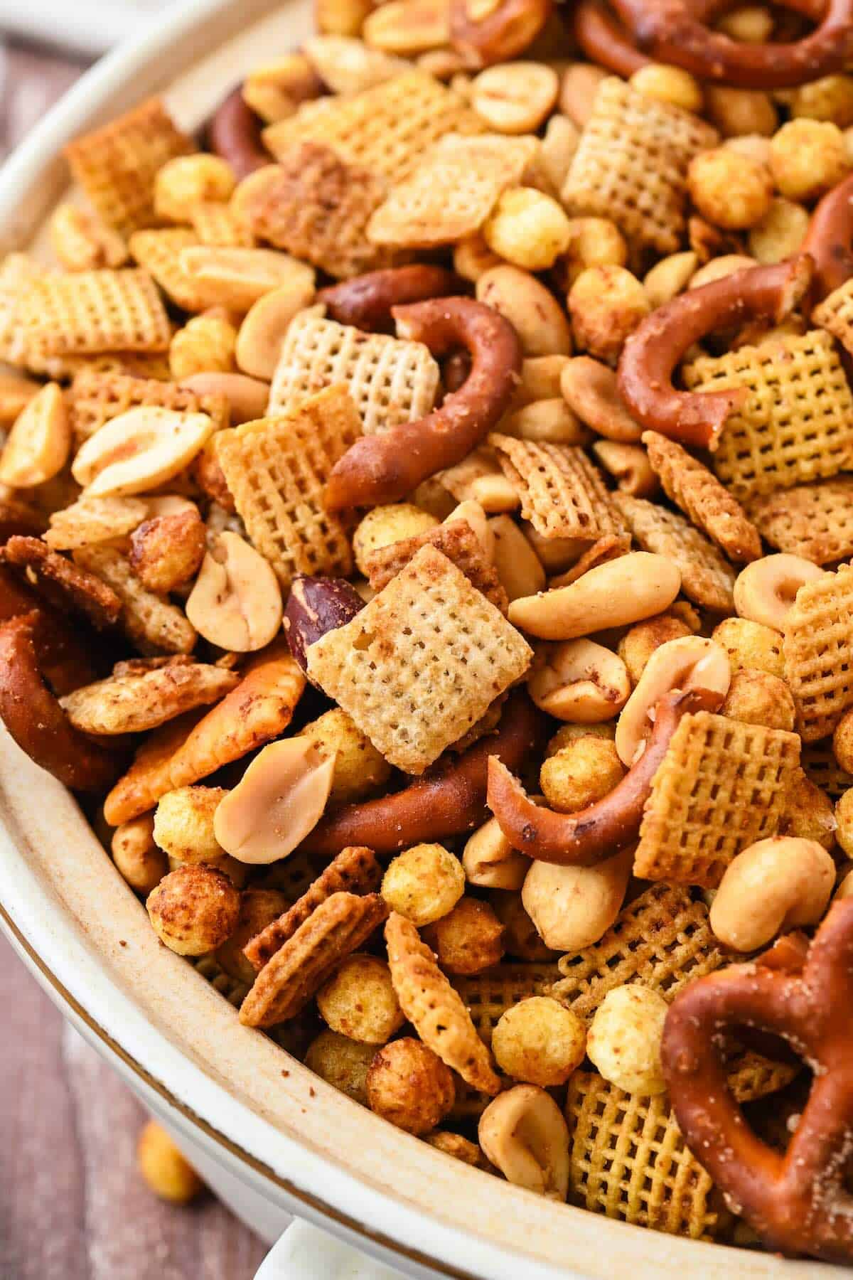 Big serving bowl of golden, crispy homemade Chex Mix on a wooden table — perfect for holiday snacking.