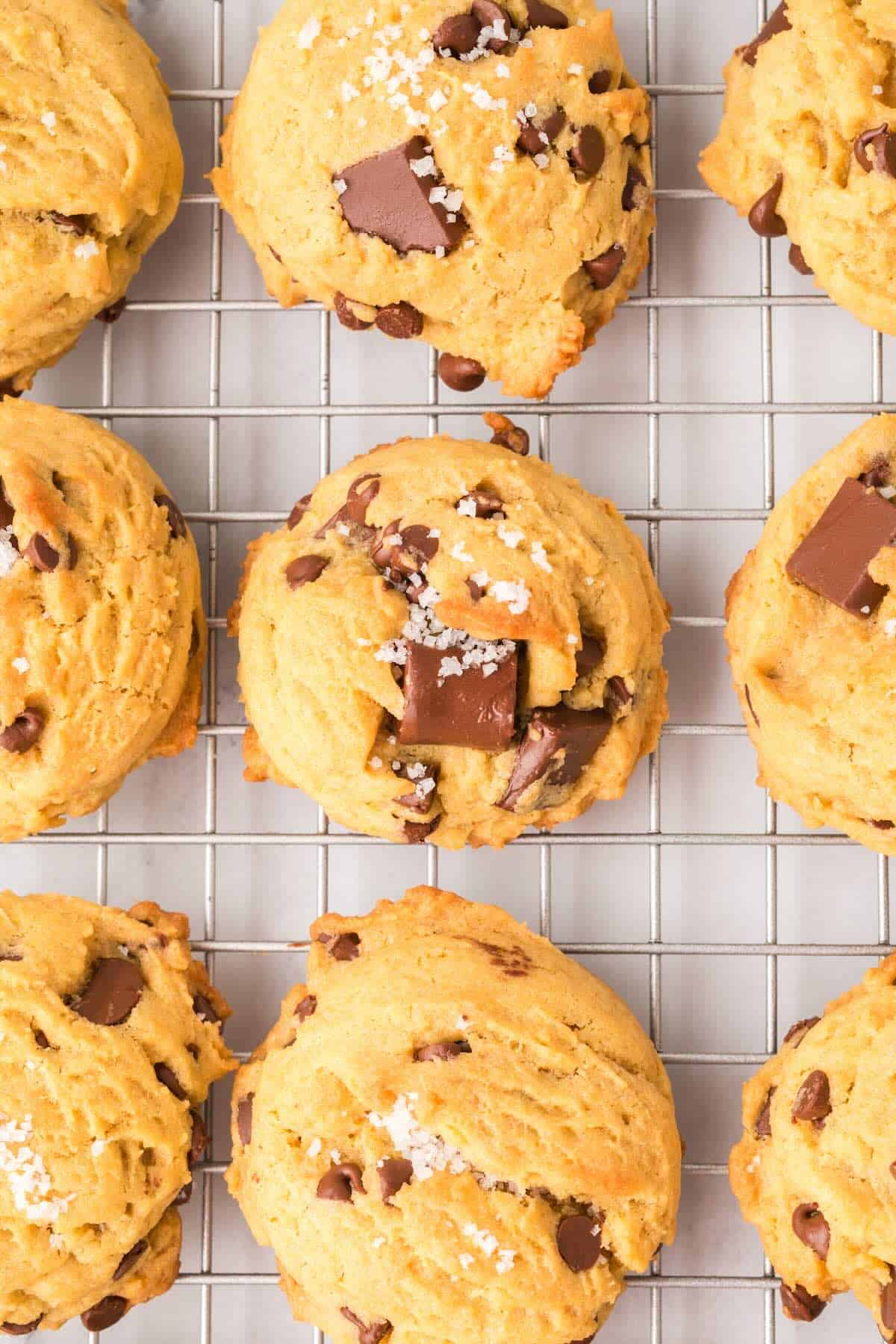 Freshly baked sourdough chocolate chip cookies cooling on a wire rack with melted chocolate bits.