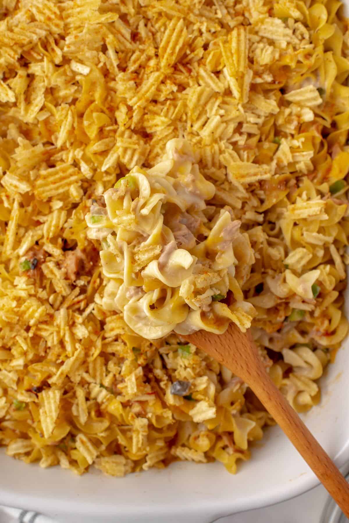 A spoonful of tuna noodle casserole with a baking dish.