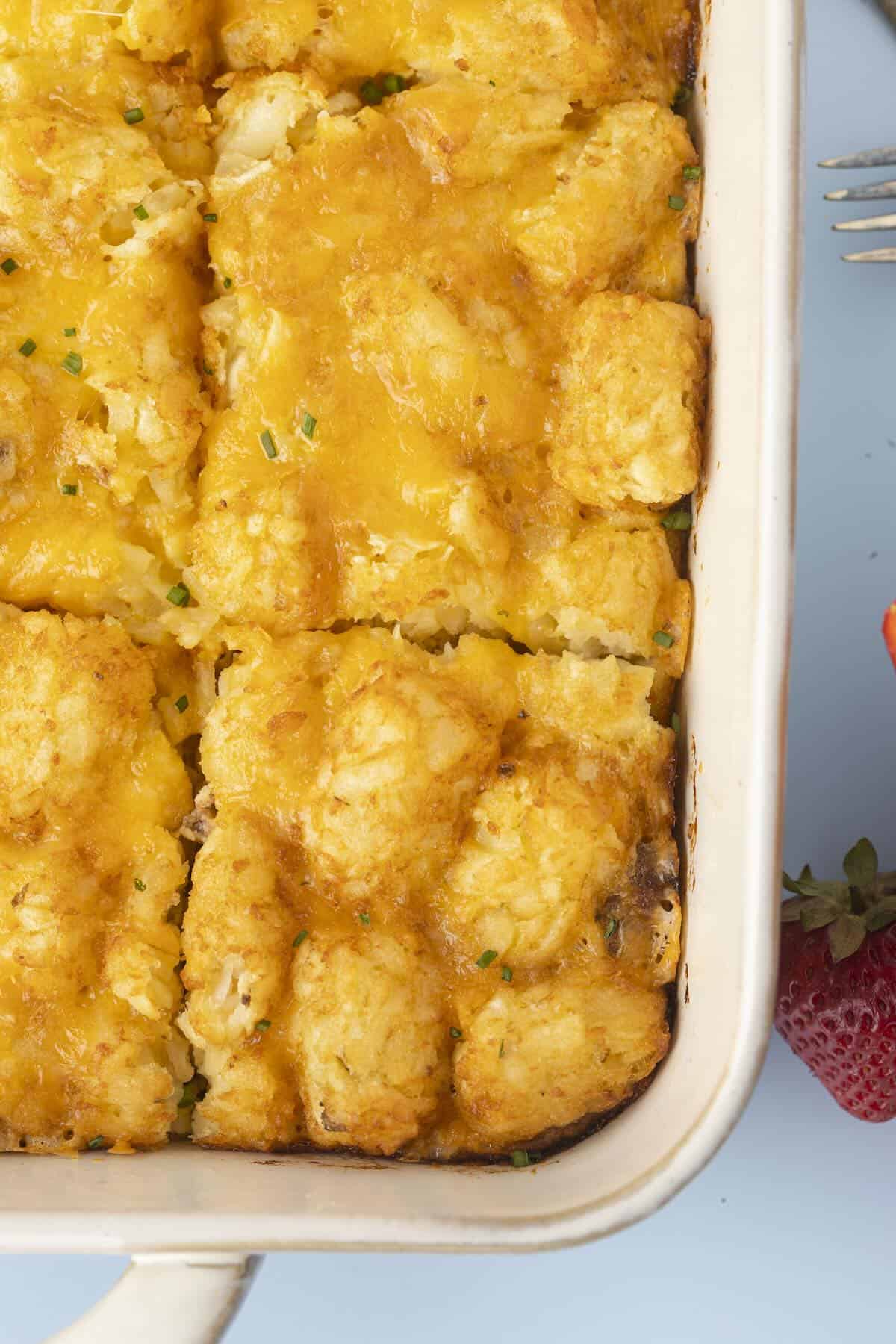 “Golden baked egg casserole without bread topped with crispy tater tots in a white baking dish.