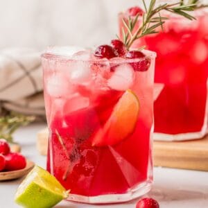 Cranberry lime margarita mocktails served on a holiday table with cranberries and greenery.
