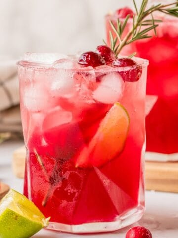 Cranberry lime margarita mocktails served on a holiday table with cranberries and greenery.