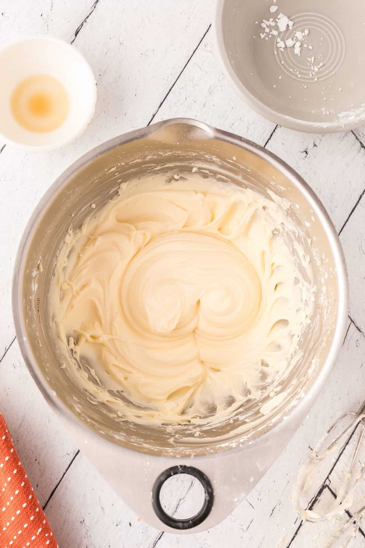 Mixing cream cheese, unsalted butter, and powdered sugar to make frosting for pumpkin snack cake.