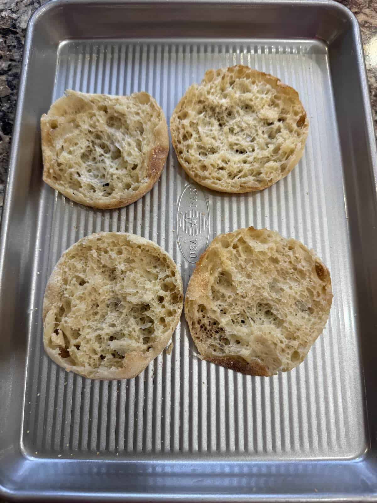English muffin halves on a sheet pan.