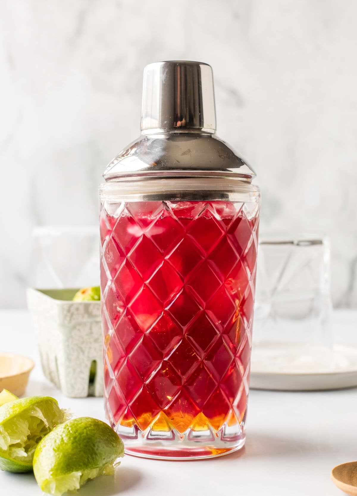 Combining cranberry juice, lime juice, and agave syrup in a cocktail shaker to make a non-alcoholic margarita.