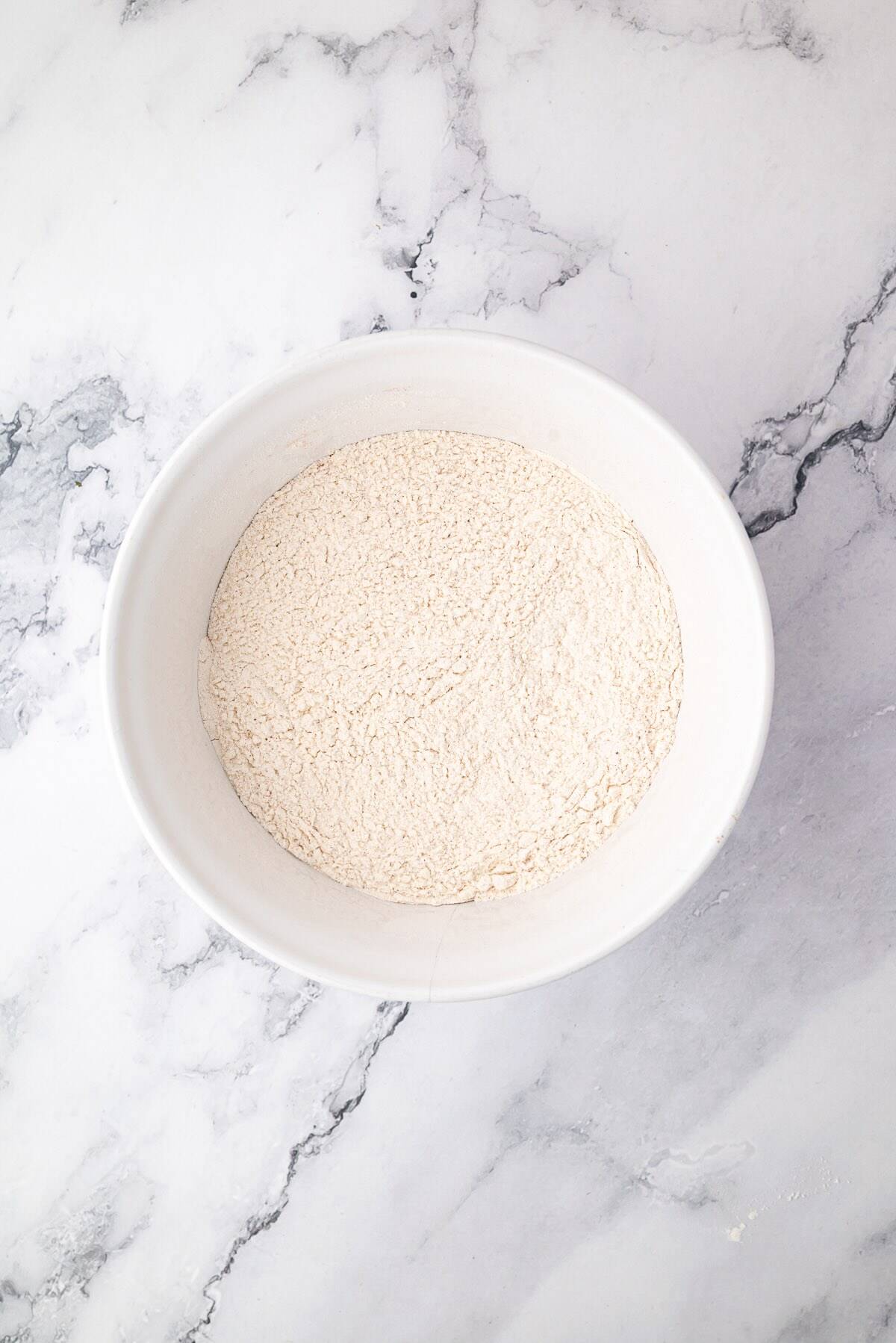 Combining flour and pumpkin pie spice in a mixing bowl for pumpkin banana bread.