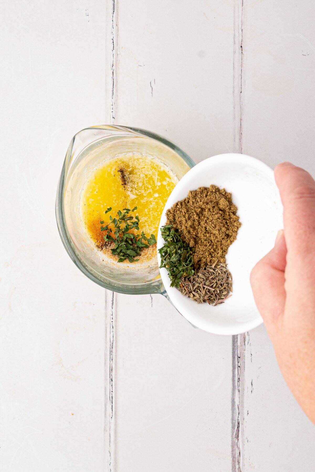 Melted butter with poultry seasoning, garlic powder, and thyme in a small bowl.