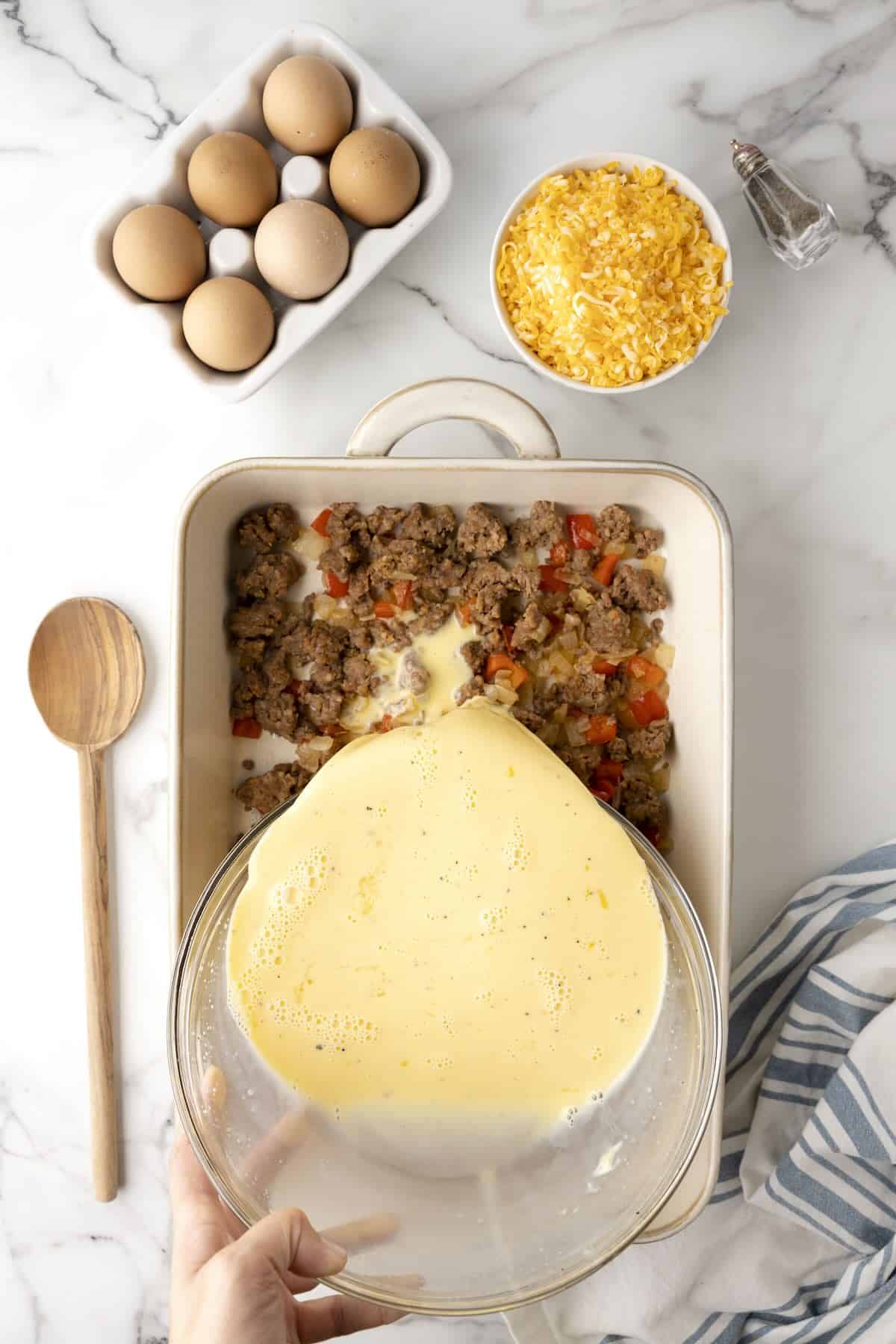 Stirring sausage, cheddar cheese, and vegetables into egg mixture for casserole.