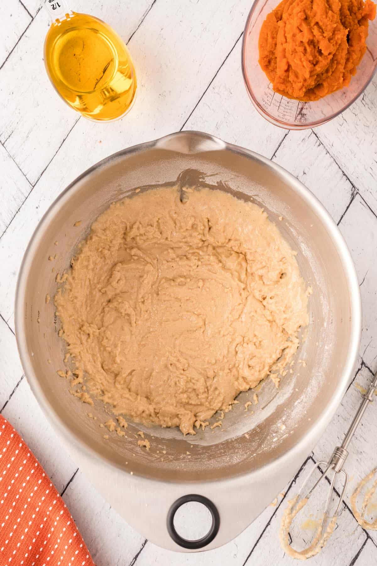 Whisking wet ingredients including pumpkin puree, eggs, and oil in a glass mixing bowl.