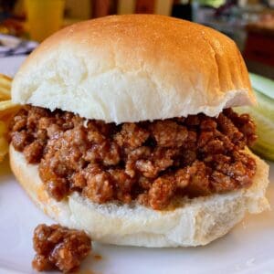 A ground beef sloppy joe sandwich on a white burger bun with meat spilling over.