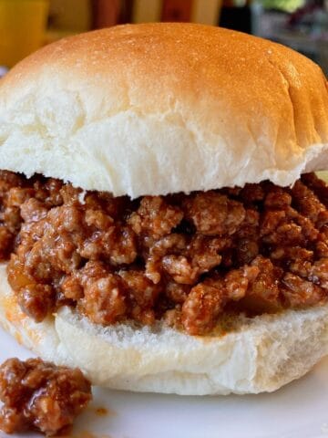 A ground beef sloppy joe sandwich on a white burger bun with meat spilling over.