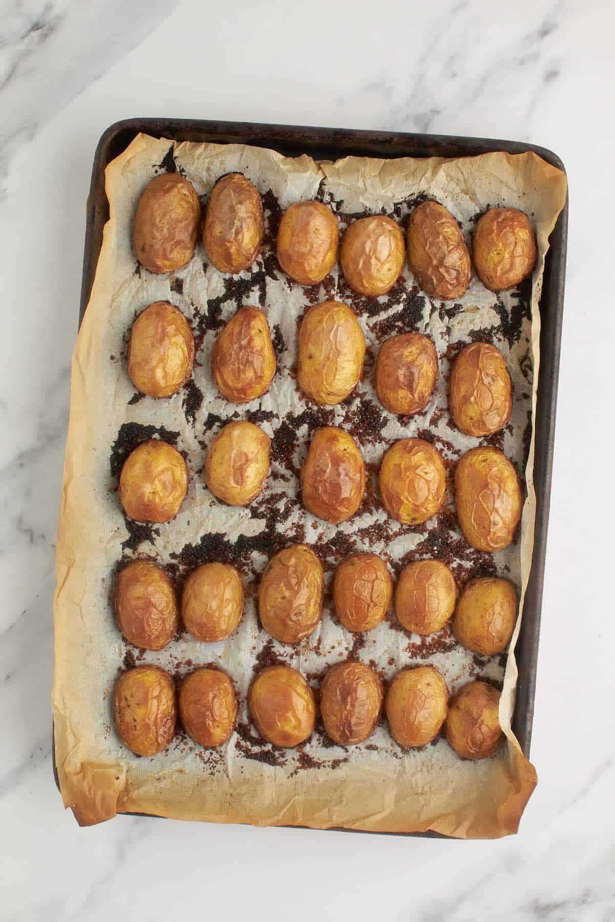 Freshly baked potatoes on a sheet pan with crispy golden Parmesan crusts.