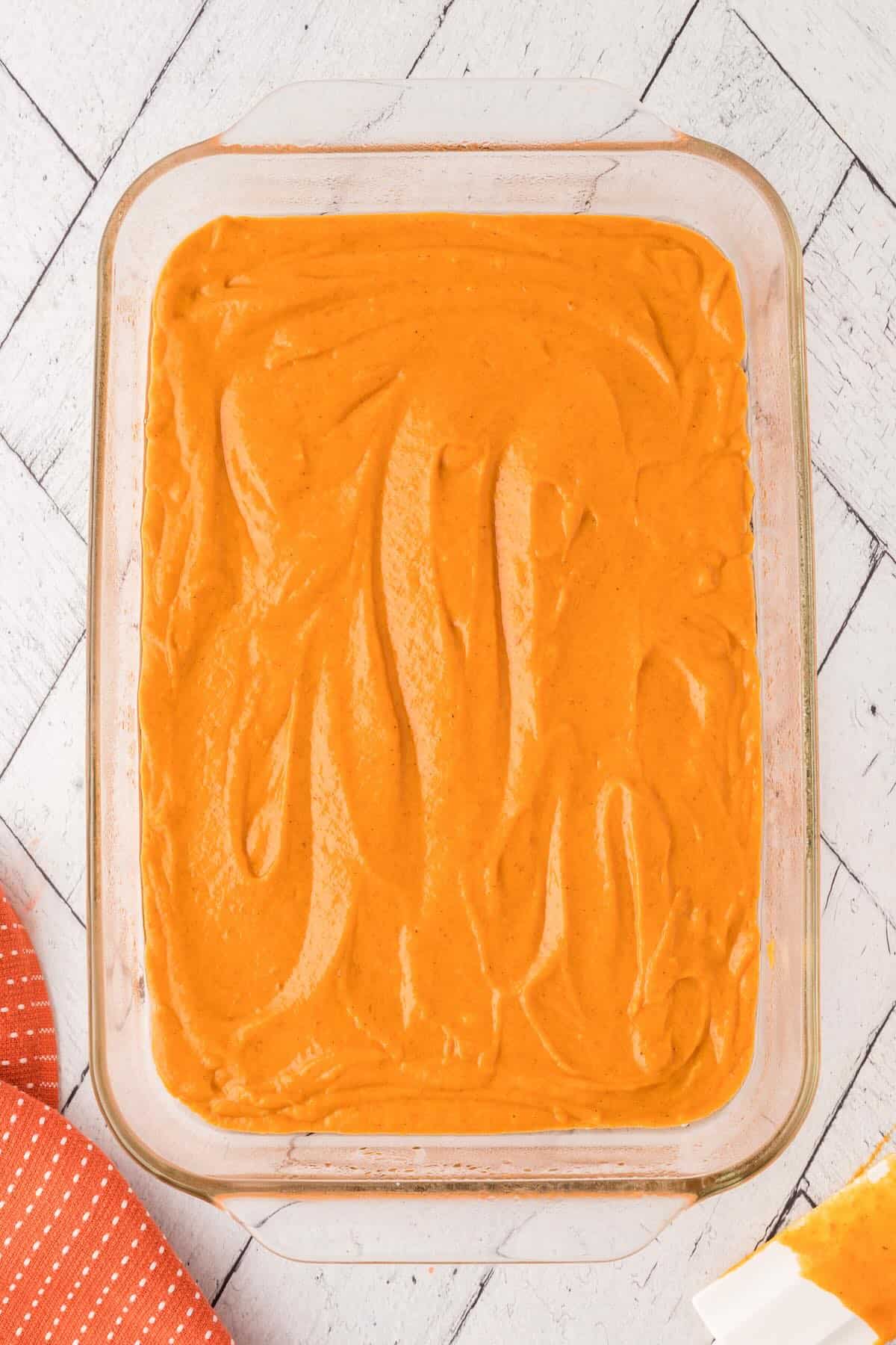 Pumpkin cake batter smoothed into a glass dish.