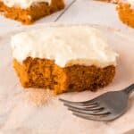 A piece of pumpkin snack cake with cream cheese frosting on a plate.