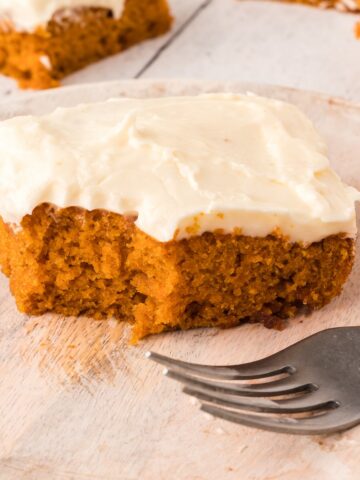A piece of pumpkin snack cake with cream cheese frosting on a plate.